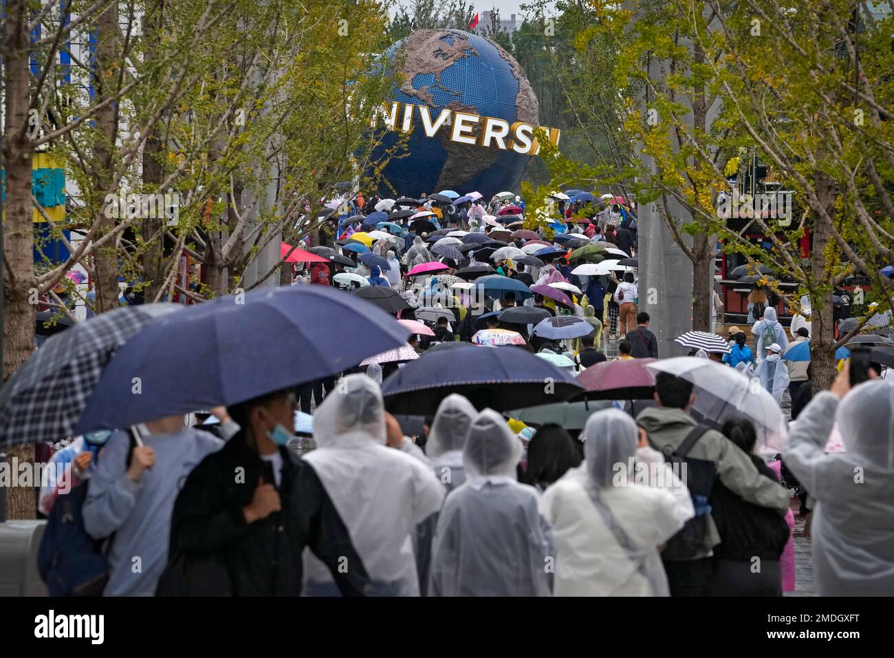 People wearing raincoats and carrying umbrellas walk through a plaza