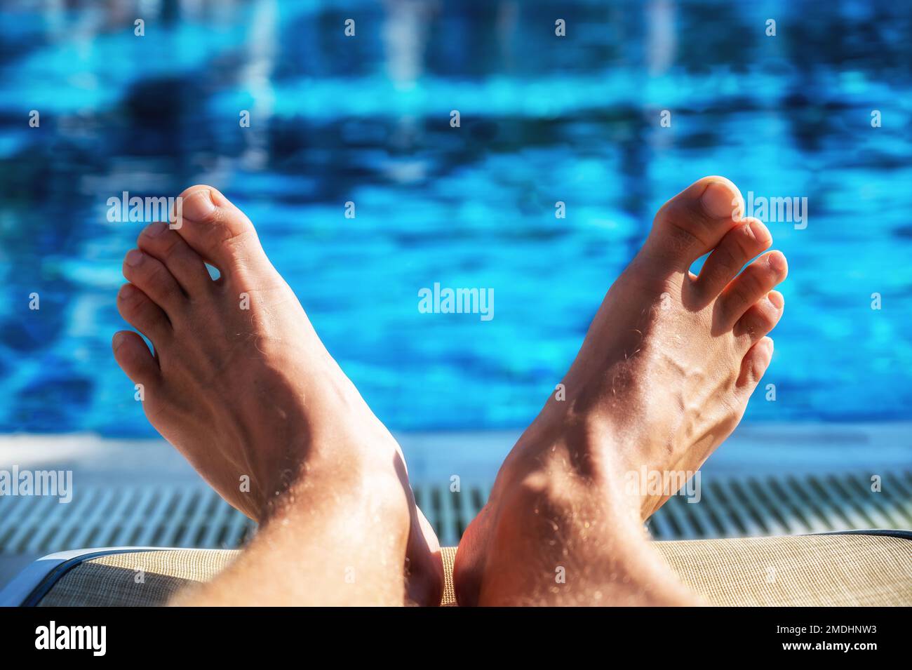 Große Füße eines Mannes auf einer Sonnenliege am Pool Stockfoto
