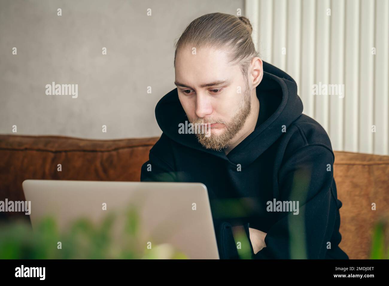 Ein attraktiver junger Mann mit Bart arbeitet an einem Laptop. Stockfoto