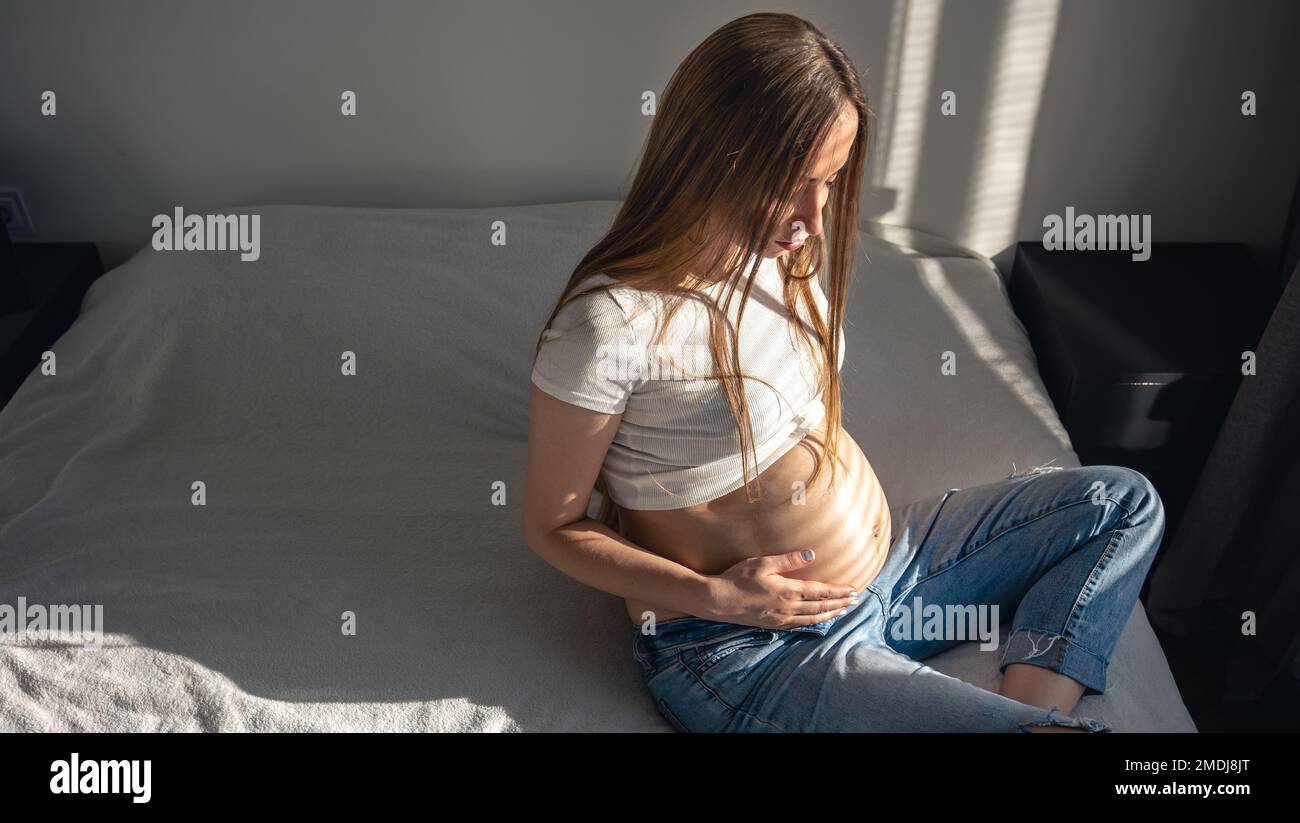 Schwangere Frau auf dem Bett im Zimmer an einem sonnigen Morgen. Stockfoto