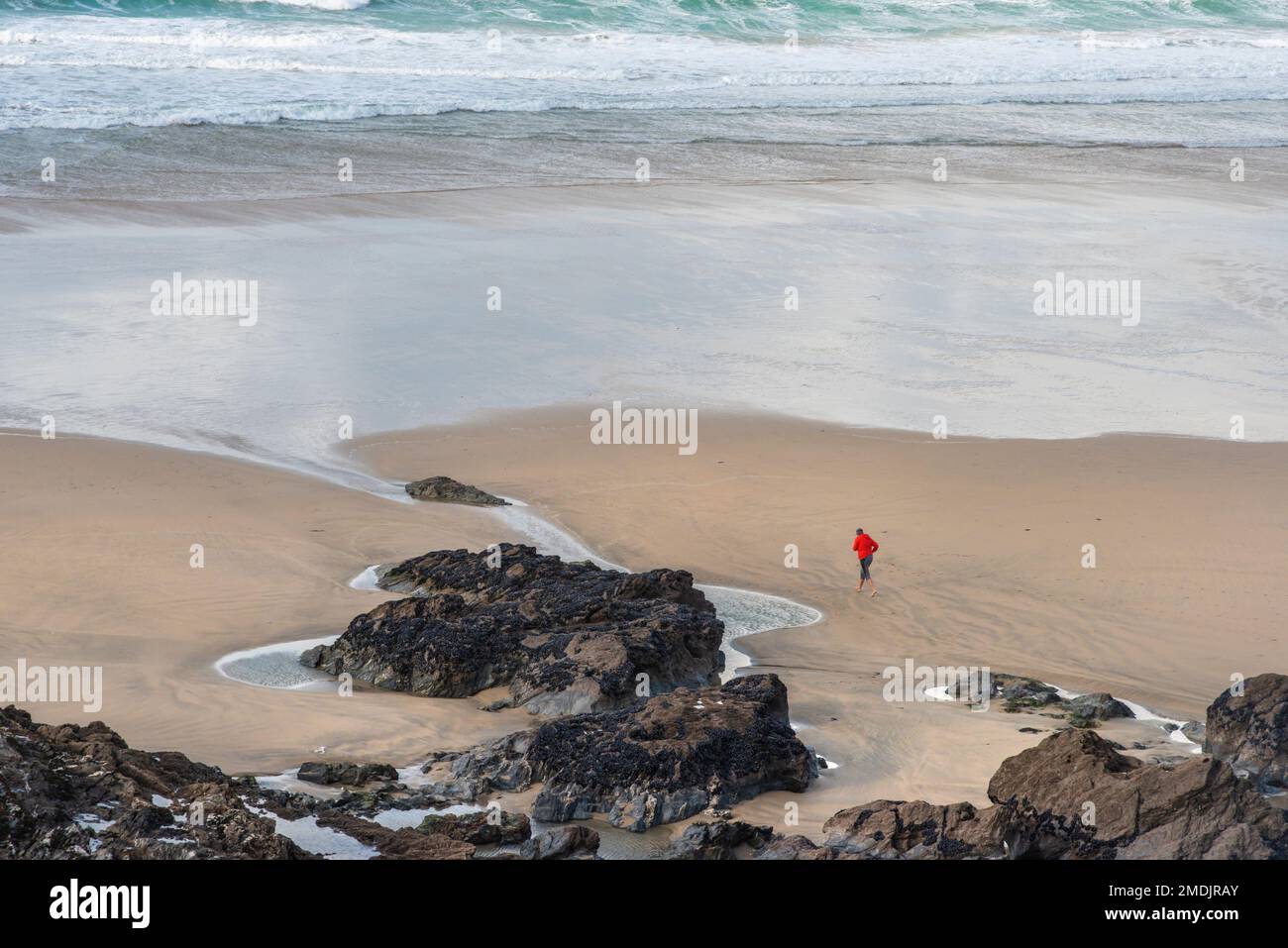 Die kleine Figur einer Person, die an einem windigen Fistral Beach in Newquay in Cornwall entlang der Küste läuft. Stockfoto