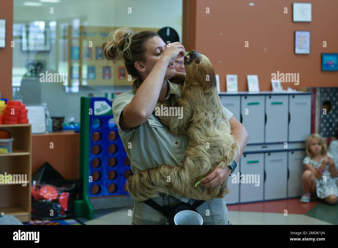 Kiana Lucero, Zoowärter des Tanganyika Wildlife Park, füttert ein Stück Brokkoli an ein Faultier namens Chewbacca, während er Kindern im Schulalter-Programm am McConnell Air Force Base, Kansas, 25. Juli 2022 etwas über Tiere beibringt. Mitglieder des Tanganyika Wildlife Park brachten Tiere in das Schulprogramm, damit die Kinder interagieren und einige der Tiere streicheln konnten, die sie im Zoo haben. Stockfoto