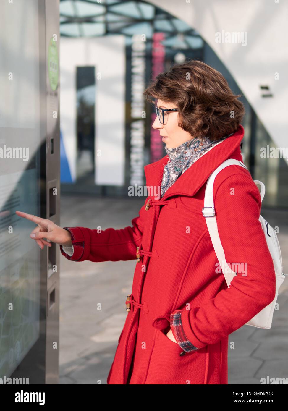 Eine lockige Frau in rotem Mantel ist auf dem Bildschirm des elektronischen Navigationsgeräts im Freien. Moderne elektronische Schalttafeln auf der Straße für den E-Commerce Stockfoto