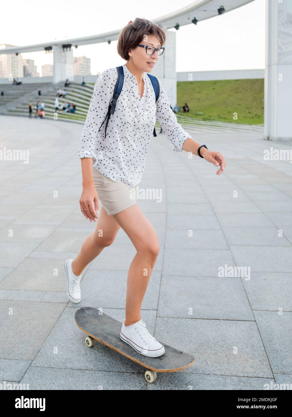 Frau fährt Skateboard auf dem Stadtplatz bei Sonnenuntergang. Sommerliche Stimmung. Neue Dinge im Erwachsenenalter lernen. Millennial lernt Skaten. Gesunder Lebensstil. Stockfoto