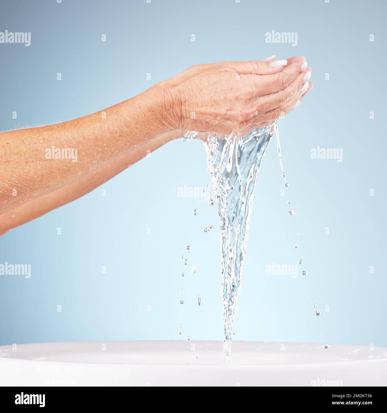 Seniorenhände, Wasser und Spritzer für saubere Hygiene, frische Mineralien oder Waschen vor dem Hintergrund eines Studios. Hand älterer Menschen, die natürliche Flüssigkeit für die Haut hält Stockfoto