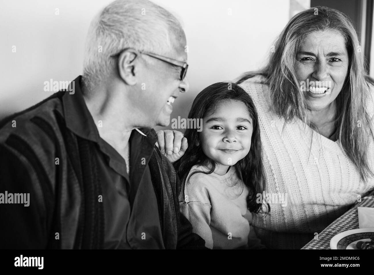 Glückliche lateinische Großeltern, die Spaß beim Essen mit ihrer Enkelin auf der Terrasse haben - Fokus auf Mädchengesicht - Schwarz-Weiß-Bearbeitung Stockfoto
