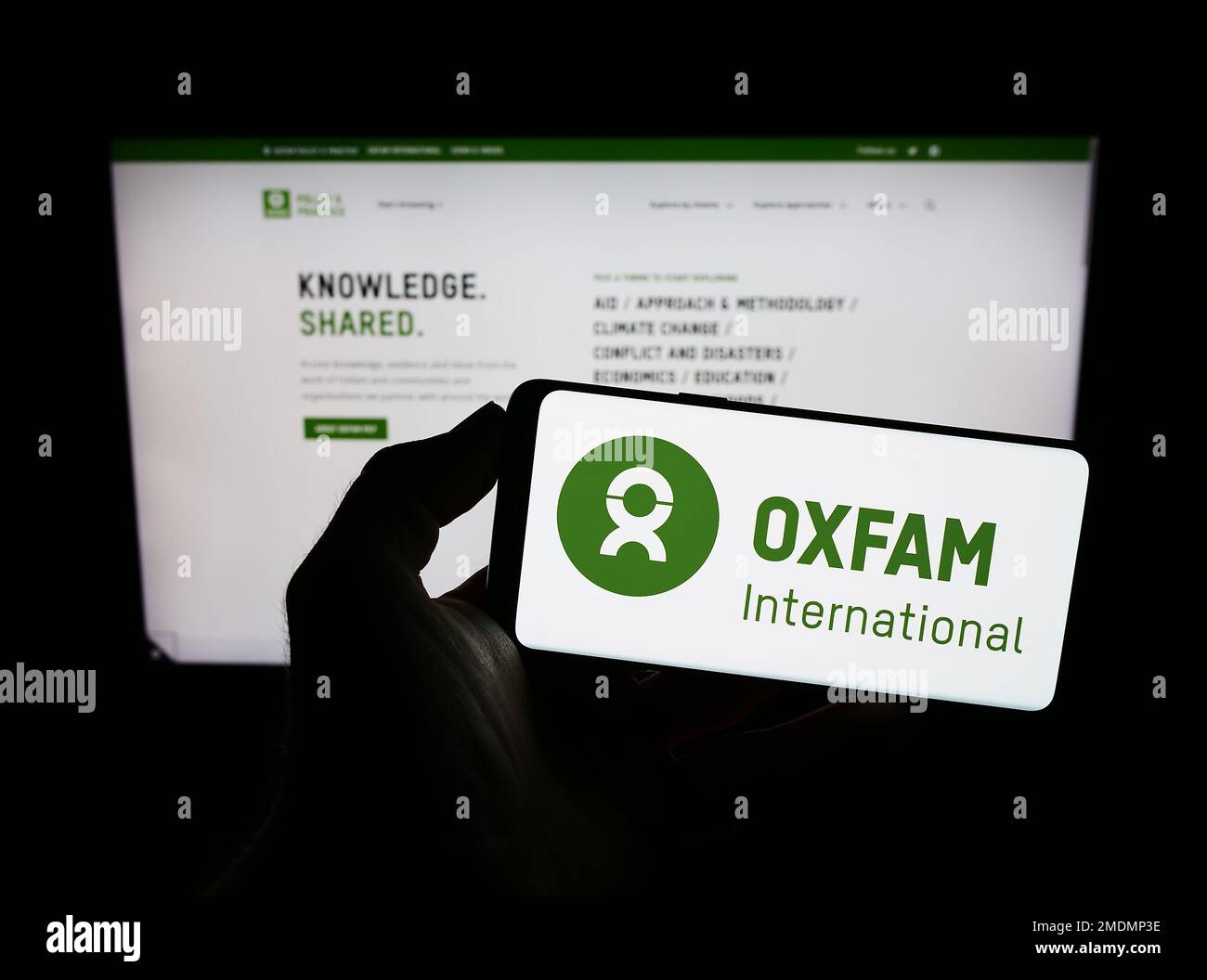 Person, die ein Mobiltelefon mit dem Logo der Confederation Oxfam International auf dem Bildschirm vor der Webseite hält. Konzentrieren Sie sich auf das Display des Telefons. Stockfoto
