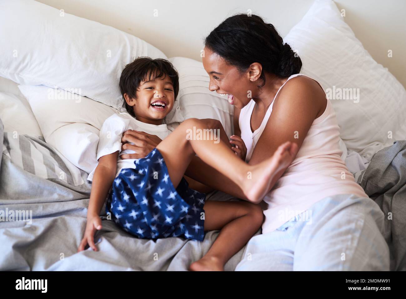 Zeit für ein paar Kitzel. Eine wunderschöne junge Mutter, die sich mit ihrem Sohn zu Hause im Bett entspannt. Stockfoto