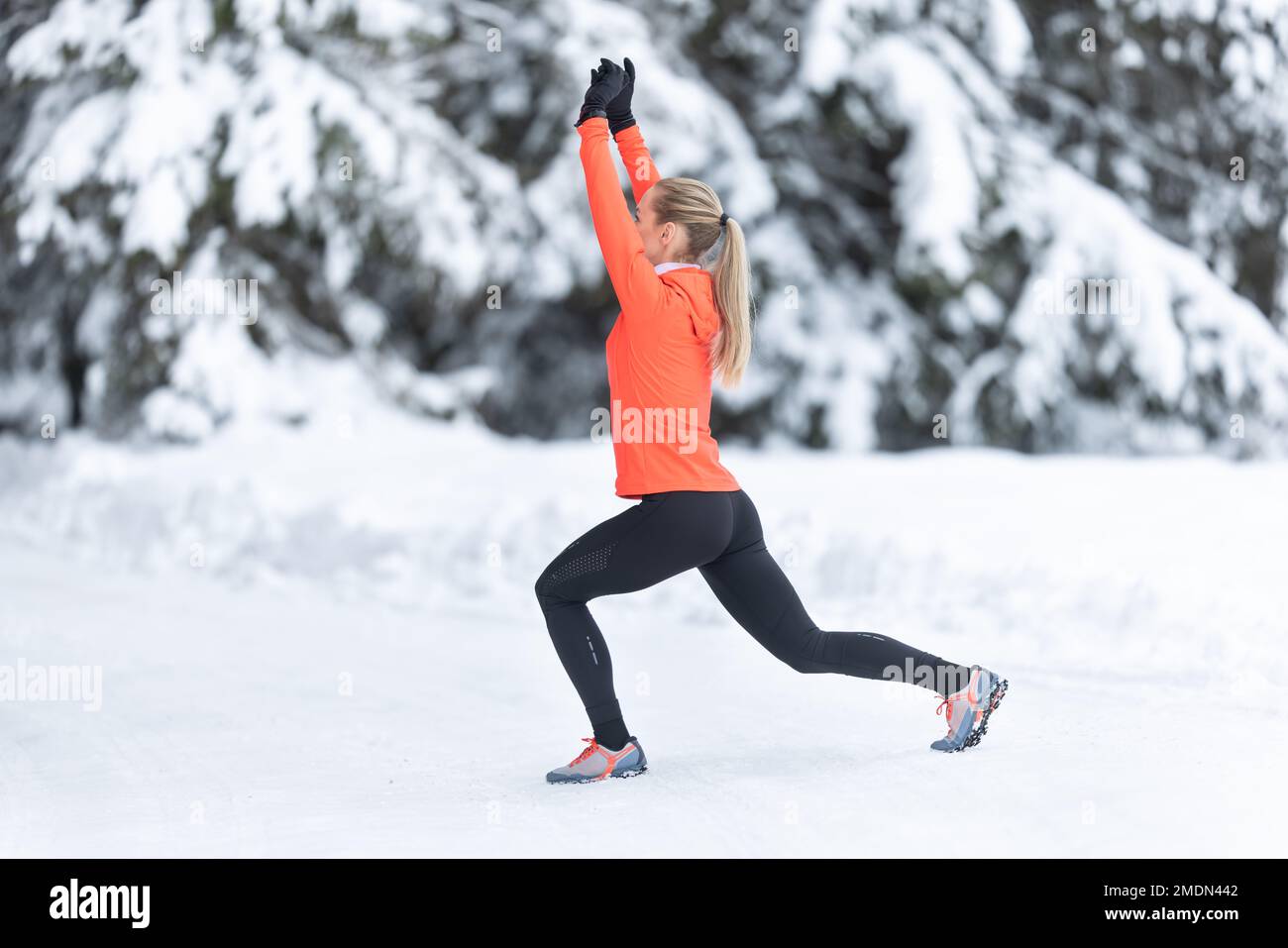 Sportliche Läuferin, die Stretching-Übungen macht und sich auf das Training im verschneiten Winterpark vorbereitet. Stockfoto