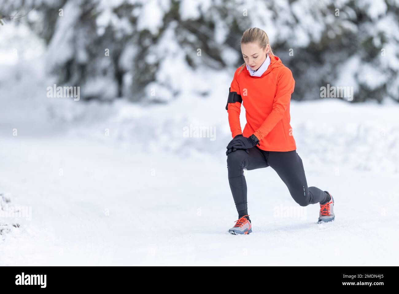 Sportliche Läuferin, die Stretching-Übungen macht und sich auf das Training im verschneiten Winterpark vorbereitet. Stockfoto