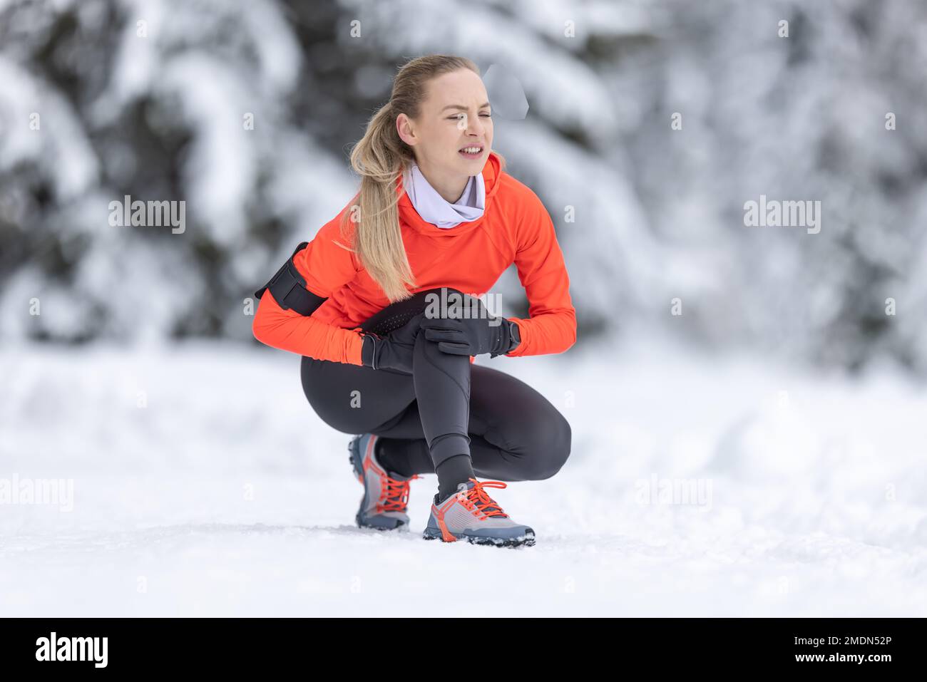 Eine junge, fit geschnittene Frau hält ein verstärktes Knie, nachdem sie ihr Kreuzband während des Langlauftrainings im Schnee während der Wintersaison gestrafft hat. Stockfoto