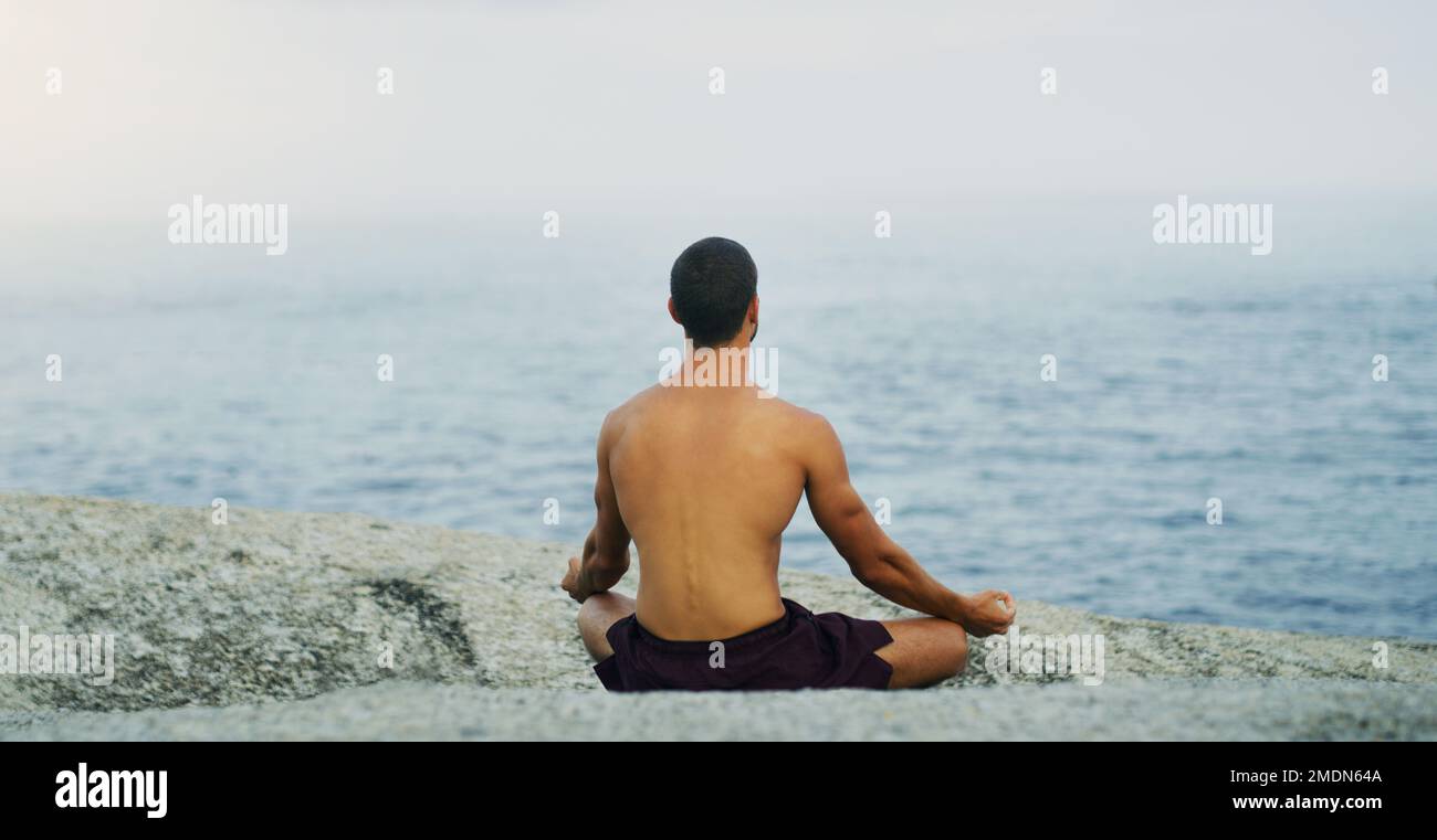 Nama, bleib hier. Rückansicht eines unbekannten Mannes, der an einem bewölkten Tag am Meer allein am Meer meditiert. Stockfoto