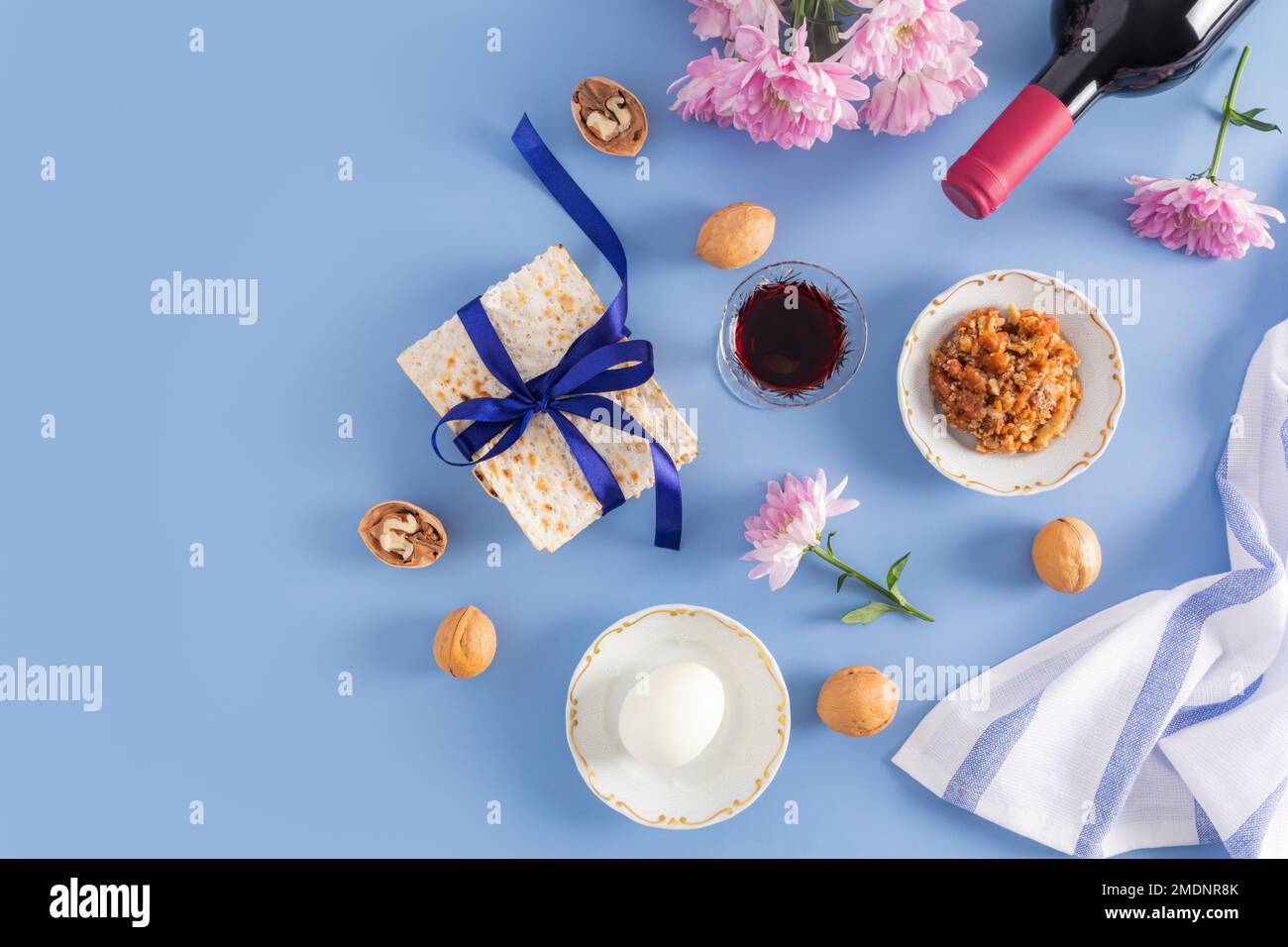 Wunderschöner blauer Hintergrund des jüdischen Pessachs. Draufsicht auf eine Flasche roter koscherer Wein, Gläser Wein, Matzah, Nüsse, Ei auf einem Teller Stockfoto