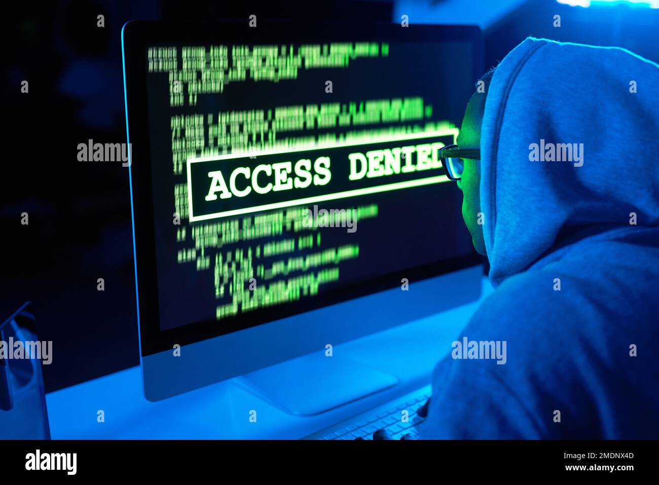 Es gibt einen Riss an jeder Wand. Ein junger männlicher Hacker knackt einen Computercode im Dunkeln. Stockfoto