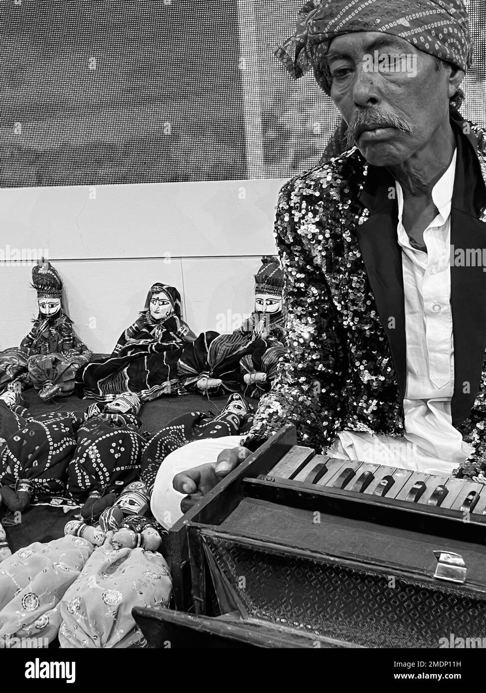 Eine vertikale Graustufenaufnahme eines alten Mannes mit einem Schal, der ein Musikinstrument hält Stockfoto