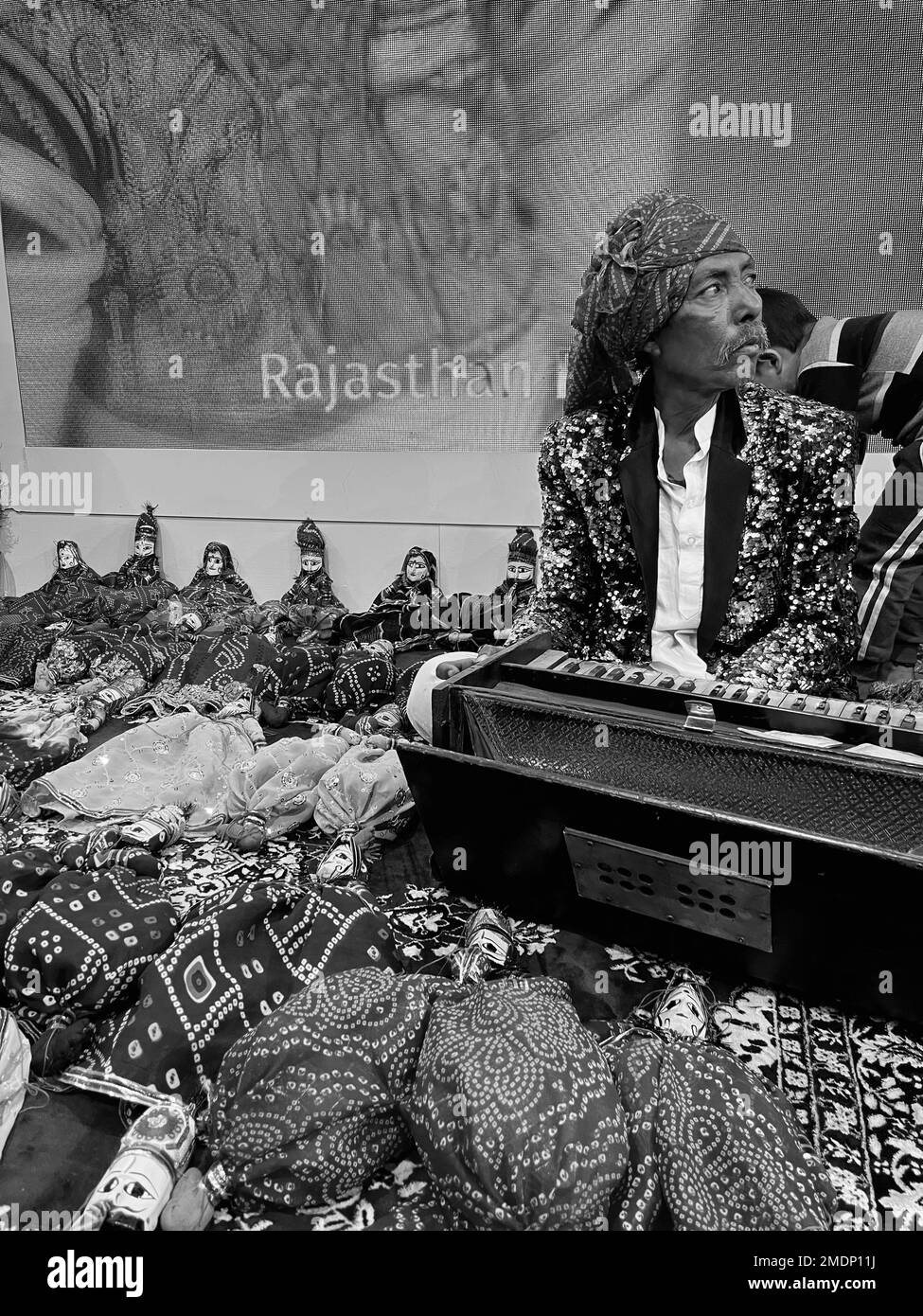 Eine vertikale Graustufenaufnahme eines alten Mannes mit einem Schal, der ein Musikinstrument hält Stockfoto