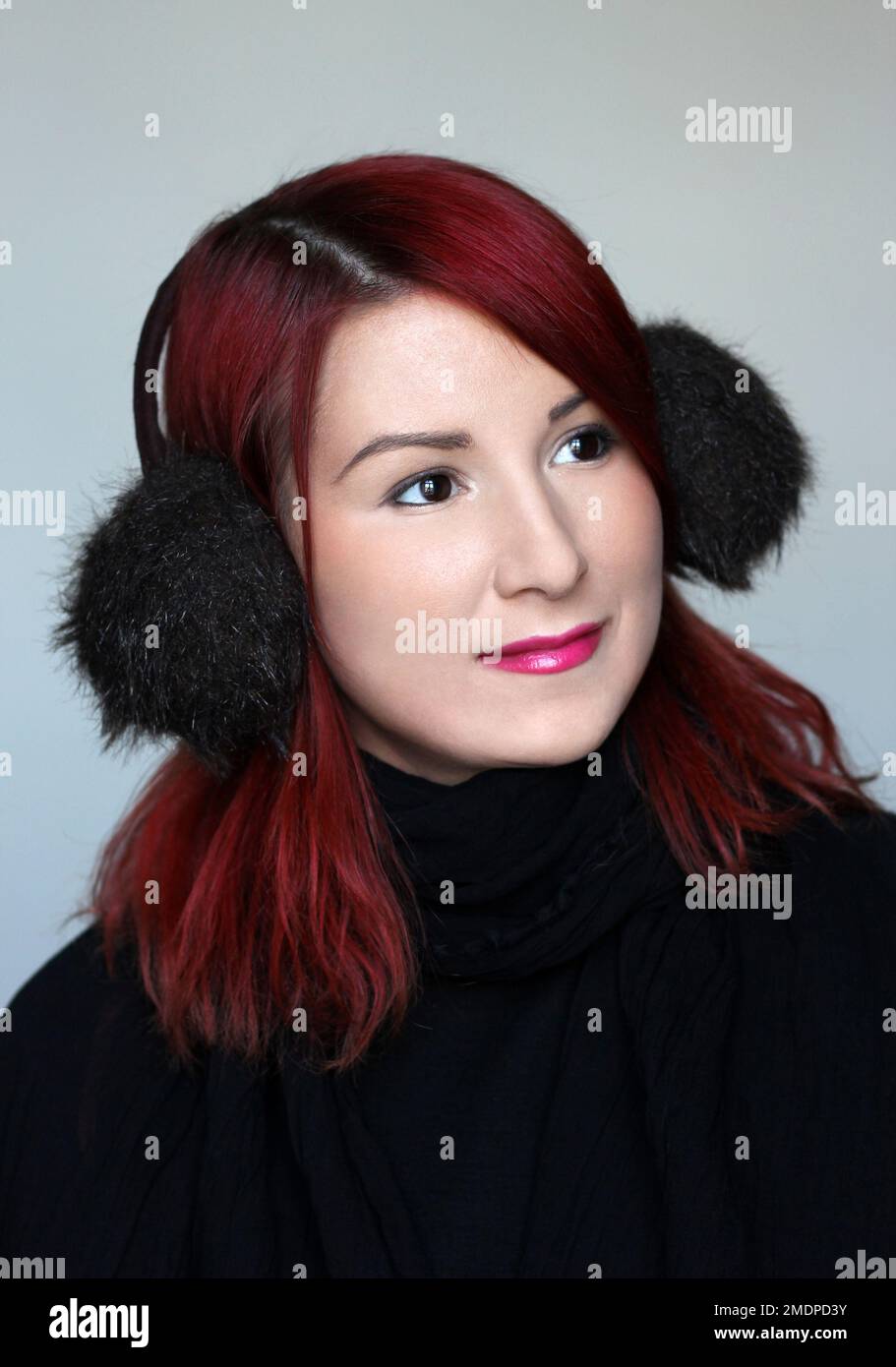 Lächelndes rothaariges Mädchen in den Pelz-Ohrenschützern und dem schwarzen Schal Stockfoto
