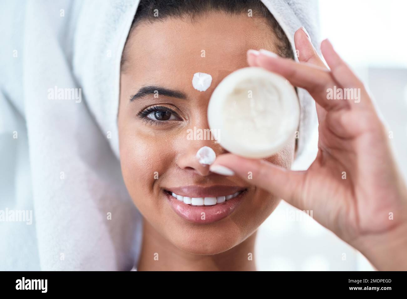 Feuchtigkeitscreme ist der Schlüssel. Eine junge Frau, die ein Schönheitsprodukt über ihr Auge hält. Stockfoto