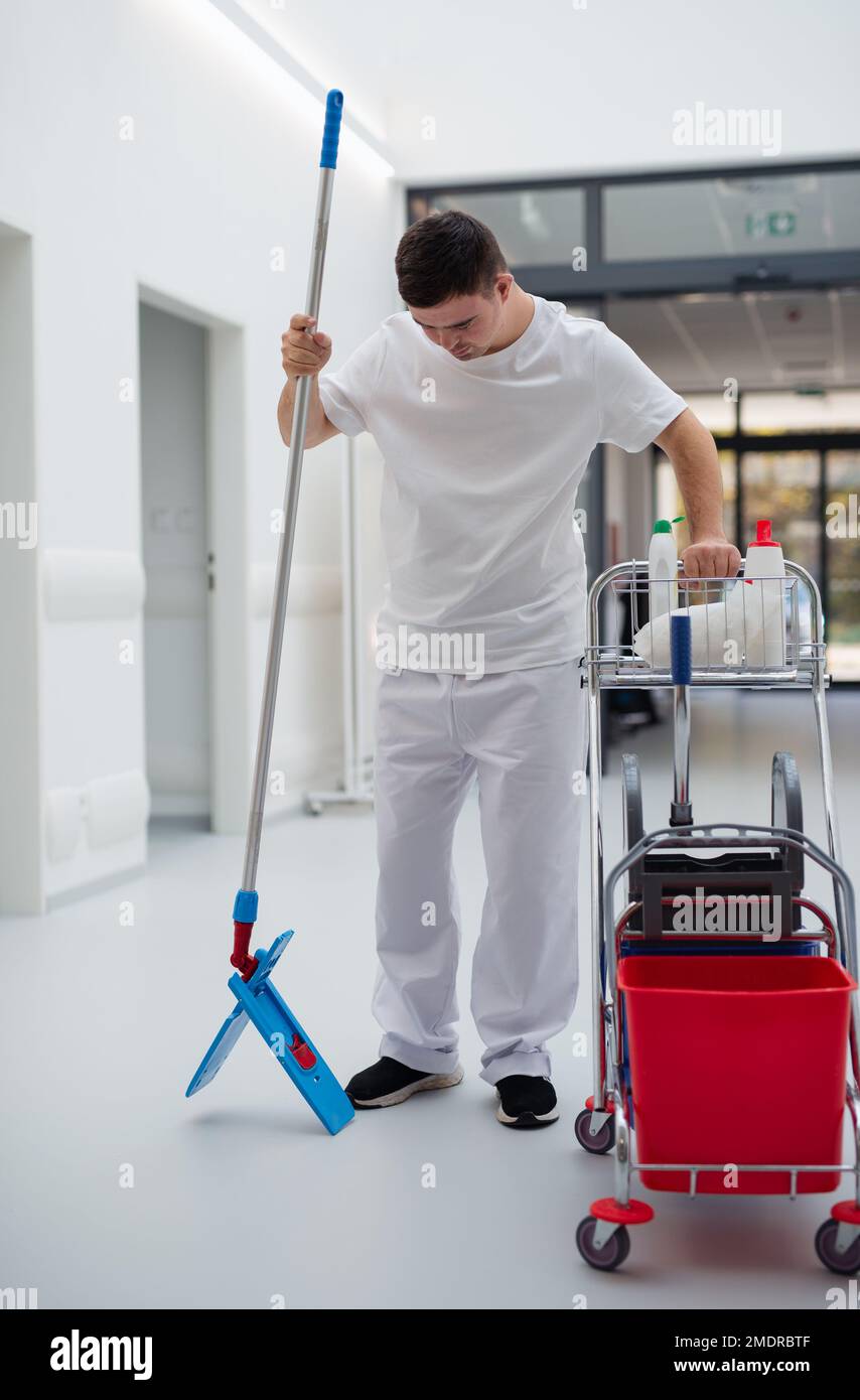 Junger Mann mit Down-Syndrom, der als Reiniger in einem Krankenhaus arbeitet. Das Konzept der Integration von Menschen mit Behinderungen in die Gesellschaft. Stockfoto