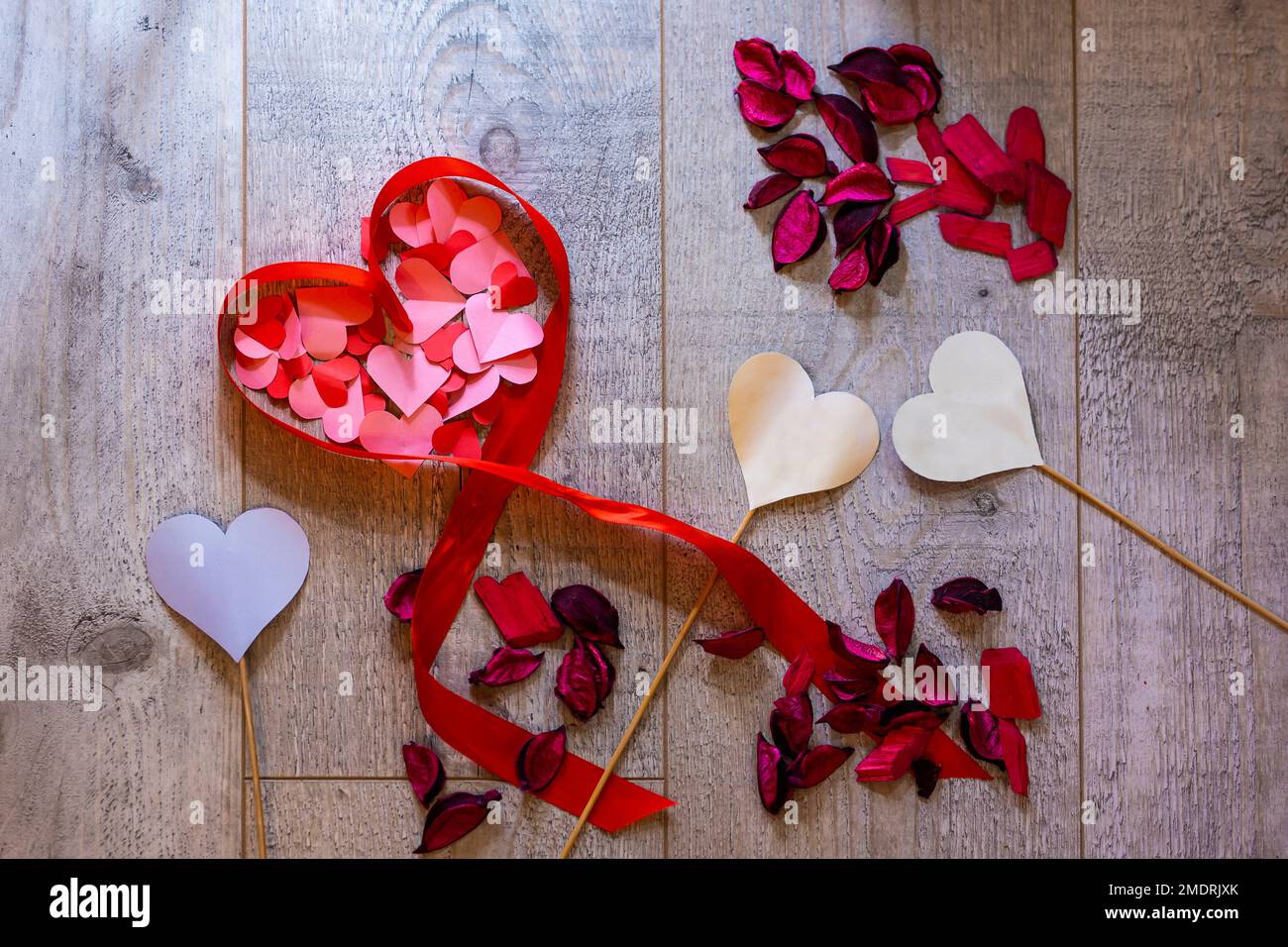 Bild mit einem Herz aus Band und vielen Papierherzen auf einem Holz-Design-Hintergrund. Das Herz ist gefüllt mit rosa und roten Papierherzen Stockfoto