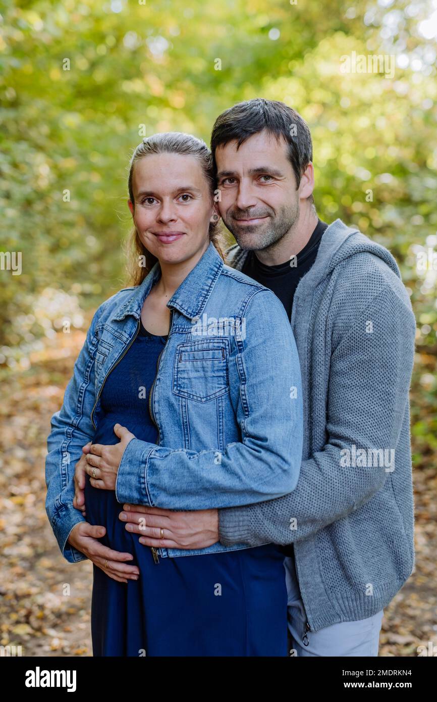 Porträt einer glücklichen schwangeren Frau und ihres Mannes, die im Wald stehen. Stockfoto