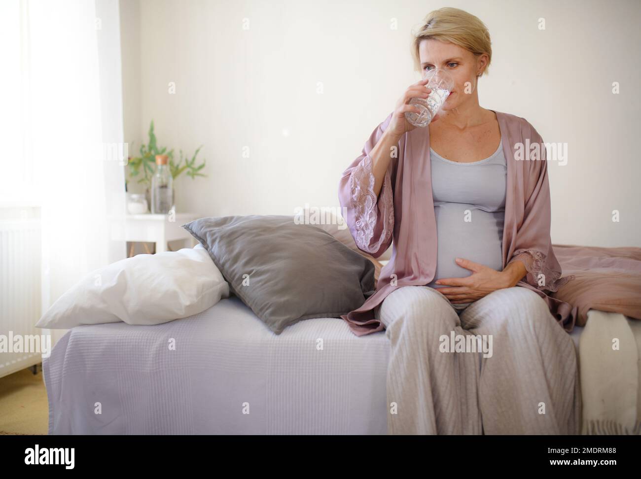 Schwangere Frau trinkt morgens Wasser in ihrem Bett. Gesunder Lebensstil und Morgenroutine in der Schwangerschaft, Concpet. Stockfoto