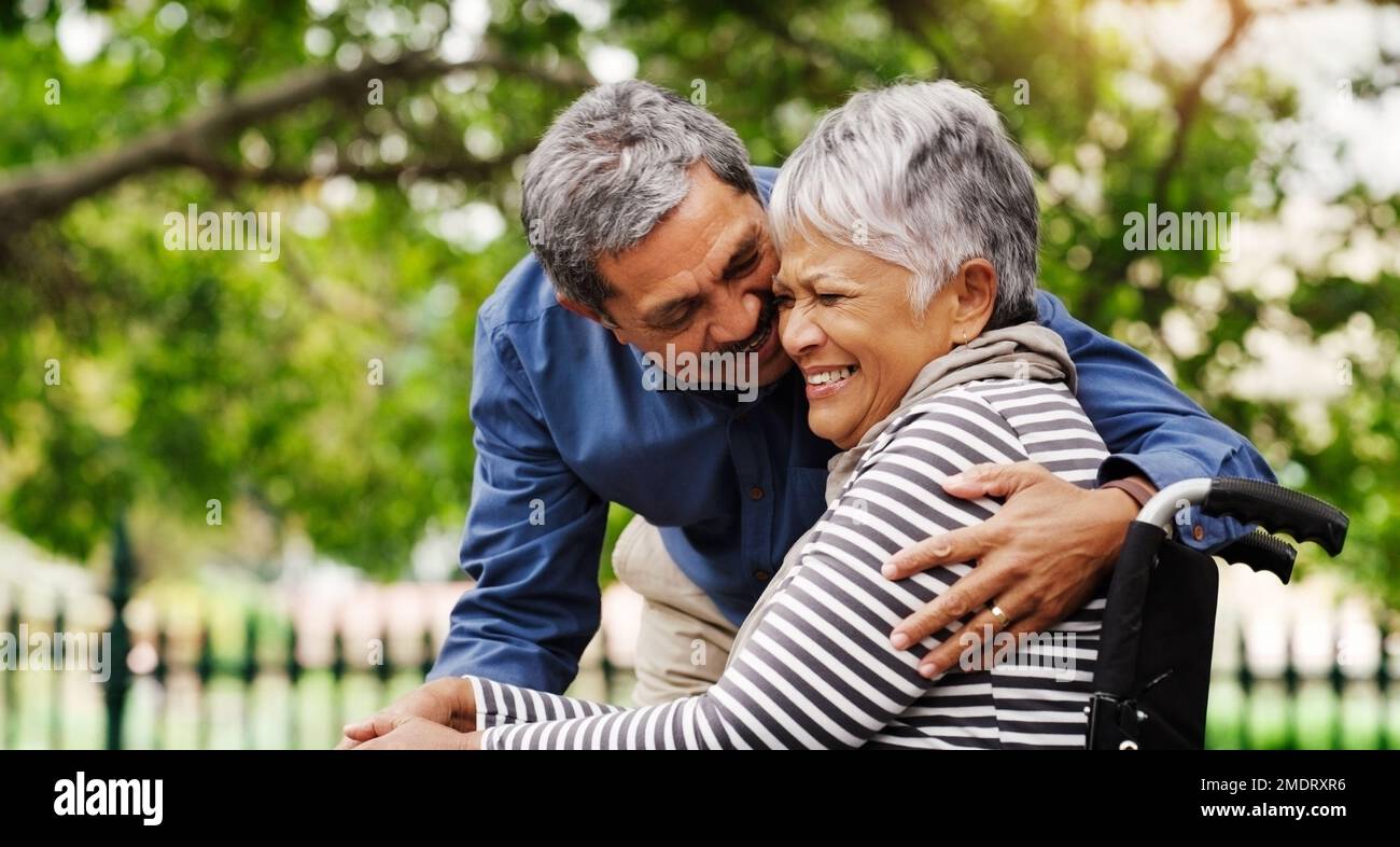 Er macht es immer leichter, mit allem umzugehen. Eine glückliche, im Rollstuhl gefesselte ältere Frau, die den Tag mit ihrem Mann im Park verbringt. Stockfoto