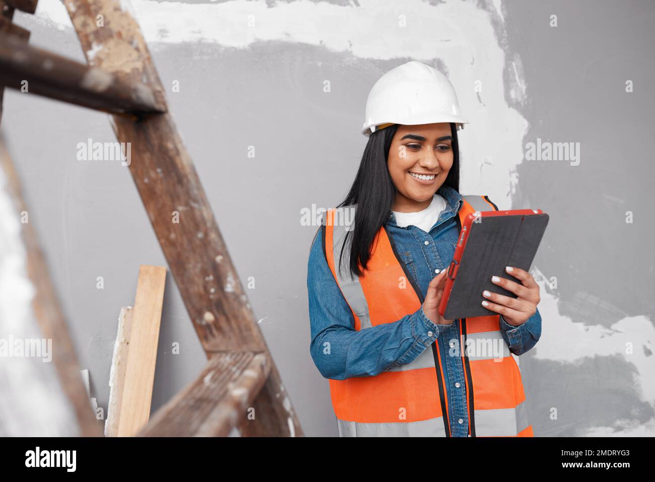 Eine junge, südasiatische Bauarbeiterin verwendet ein Tablet, um ein Projekt zu protokollieren Stockfoto