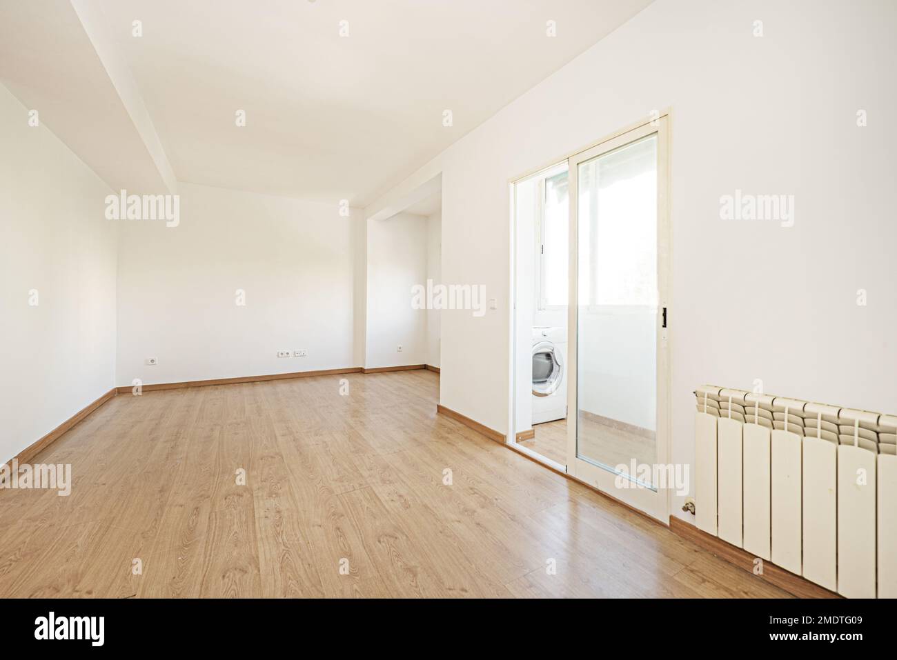 Leeres Wohnzimmer eines Hauses mit Eichenlaminatboden mit passenden Sockelleisten und Türen, geschlossene Terrasse mit doppelverglaster Aluminiumtür mit einem Stockfoto