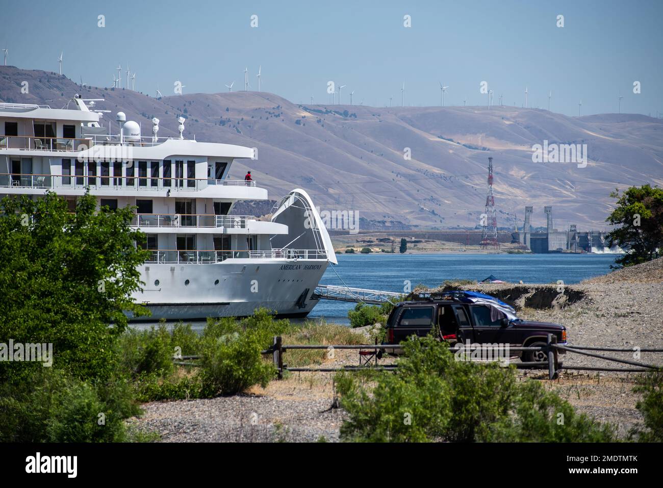 Ein Kreuzfahrtschiff, das flussaufwärts auf dem Columbia River unterwegs ist, wartet bei Rufus Landing, gleich stromabwärts vom John Day Dam, Juli 26, während die Schleuse des Staudamms vorübergehend geschlossen wird, da ein Führungsrad am stromaufwärts gelegenen Seitentor des Staudamms gebrochen ist. Am selben Abend nahm das Corps die Schiffssperren wieder auf, und zwar mit einem schwimmenden Schott – einer Wand, die mit einem Schlepper hinein- und herausgeschoben werden kann und im Wesentlichen als temporäres Tor verwendet wird. Derzeit dauert die Sperrung von Schiffen, die in der Regel etwa 45 Minuten dauert, doppelt so lange. Die Führungsräder, von denen zwei an jeder Seite des Tores befestigt sind, fungieren als Rollen, die diese Rolle spielen Stockfoto