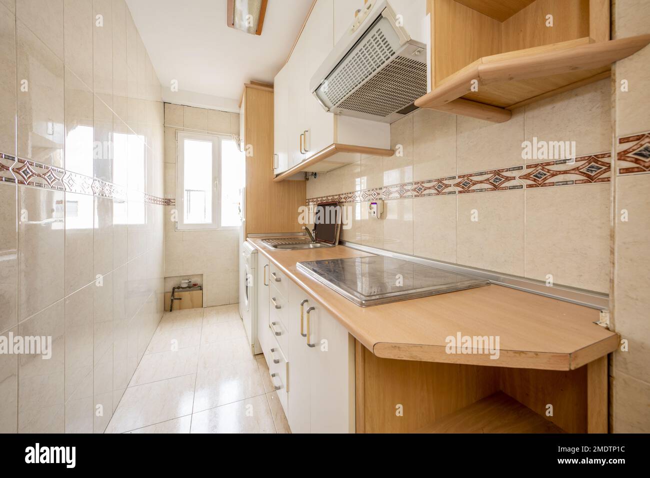 Kleine Küche mit weißen Wänden und Grundeinheiten mit Holzdetails auf der Arbeitsfläche und Maisleisten und einem Aluminiumfenster im Hintergrund Stockfoto