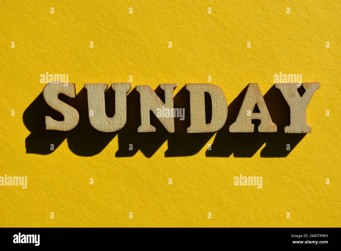Sonntag, Wort in 3D hölzernen Buchstaben isoliert auf gelbem Hintergrund Stockfoto