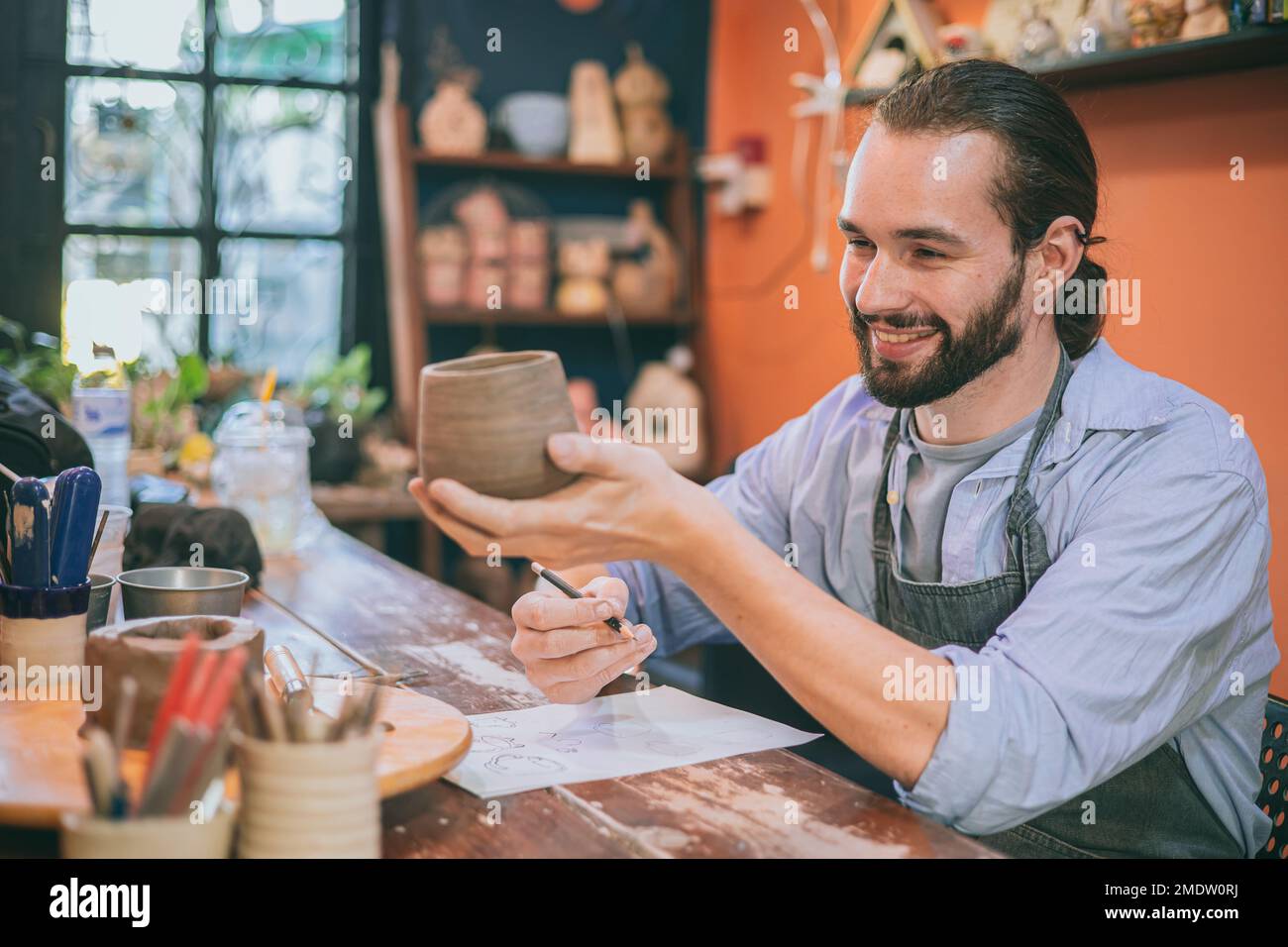 Ein kreativer Künstler aus Keramik, der sich die letzte Handwerkskunst anschaut, cray Cup, fröhliches Lächeln. Mann ist stolz auf das Designprodukt. Stockfoto