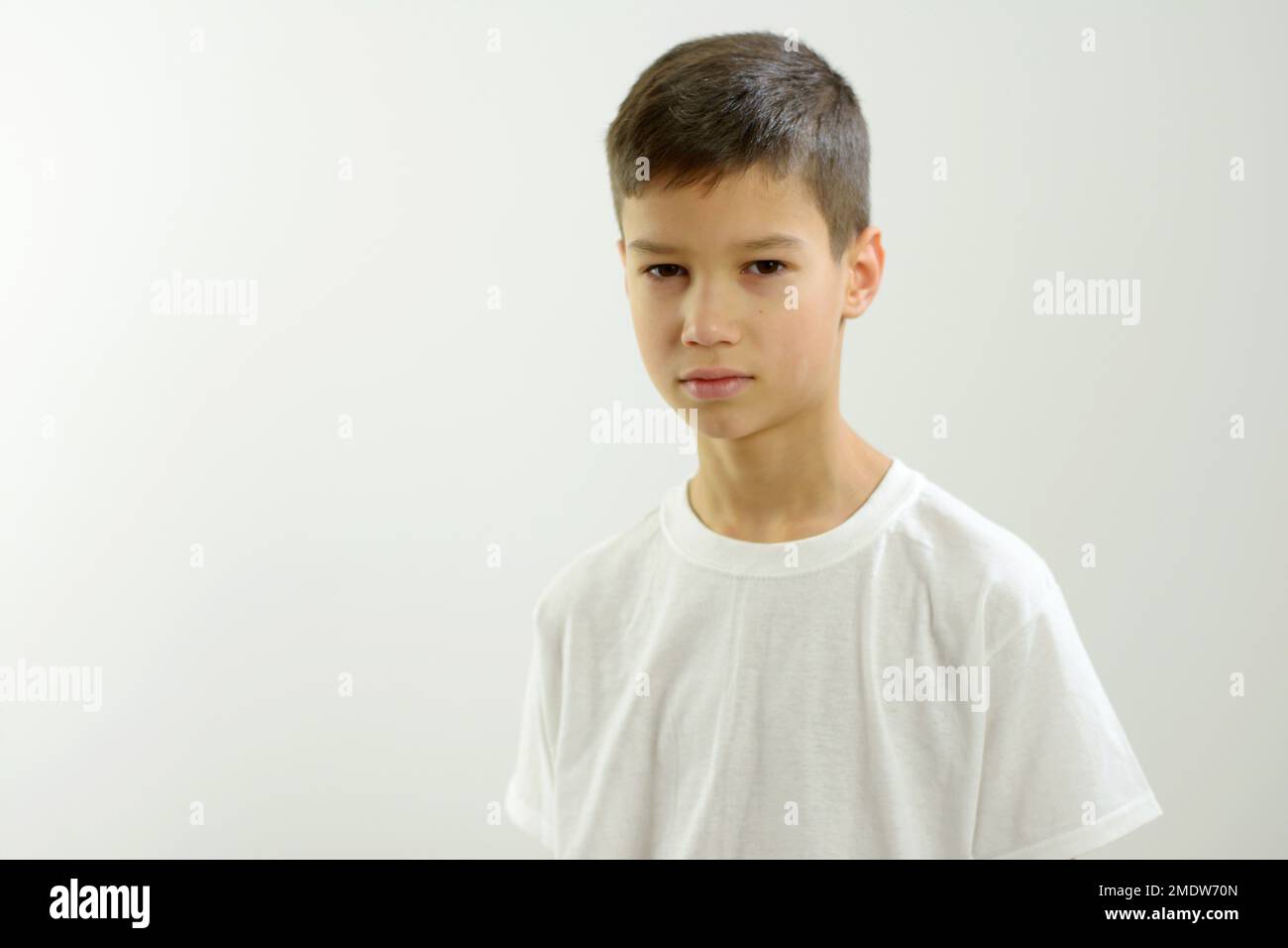 Ein 8-10-jähriger Junge sieht in den Rahmen, da ist Platz für Text auf weißem Hintergrund. Er ist ein wenig traurig. Er hat schmale orientalische Augen. Schöne Lippen, ordentlich frisiert dunkles Haar, weißes T-Shirt, ein wenig tadelnswert Stockfoto