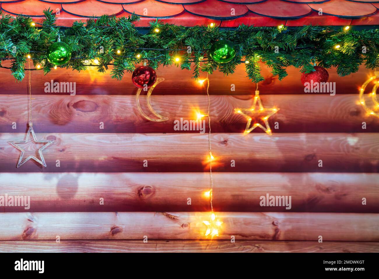 Weihnachtsbälle, Spielzeug und leuchtende Girlanden auf einem künstlichen Fichtenzweig und Holzhintergrund. Stockfoto