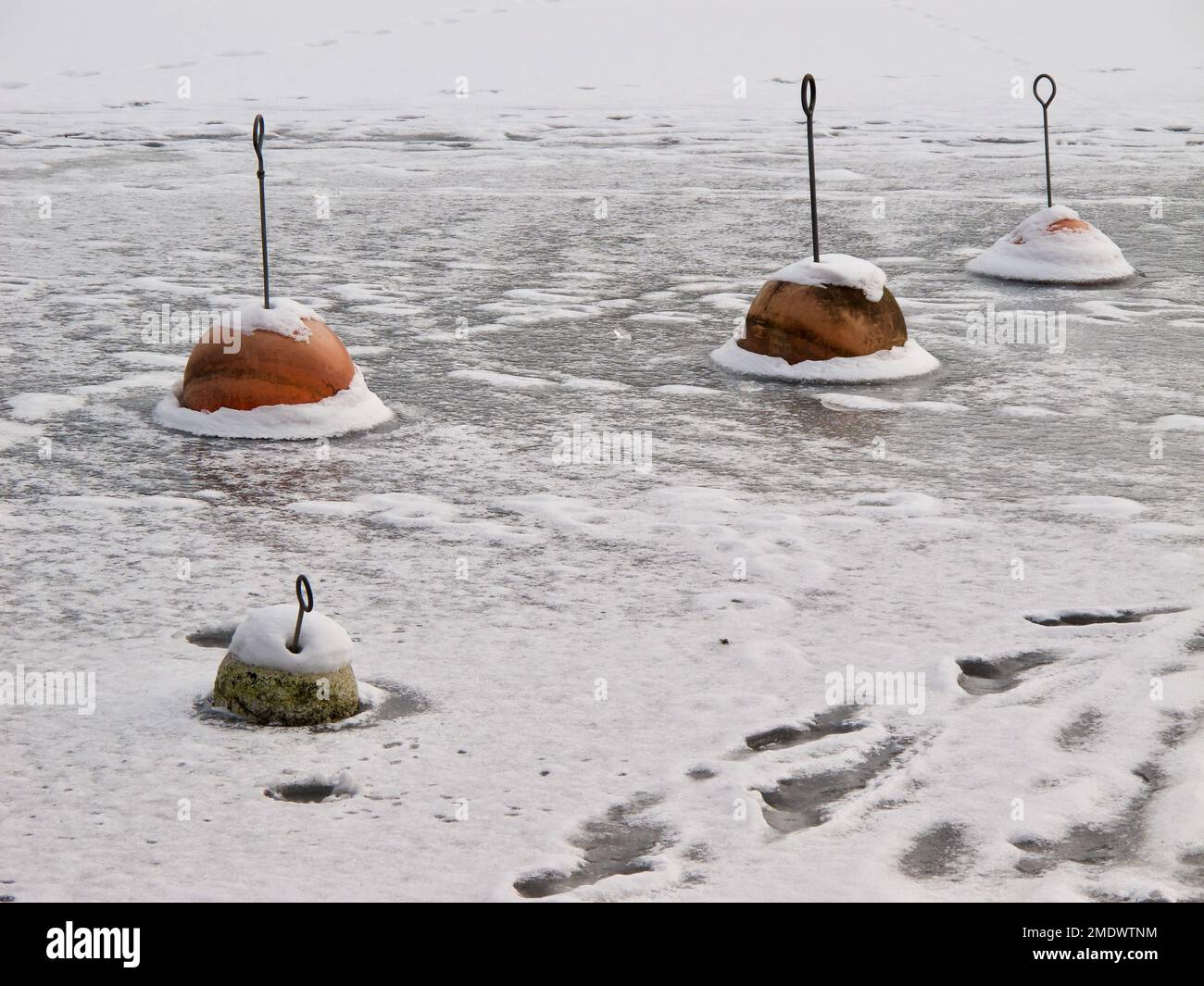 See mit roten Ankerbojen, die im Winter im Eis gefroren sind. Stockfoto