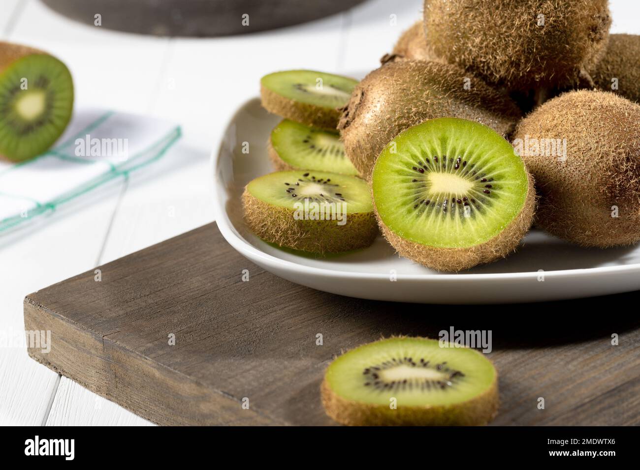 Nahaufnahme von frischer Kiwi und Scheiben auf weißem Teller auf weißem Holzhintergrund. Selektiver Fokus. Stockfoto