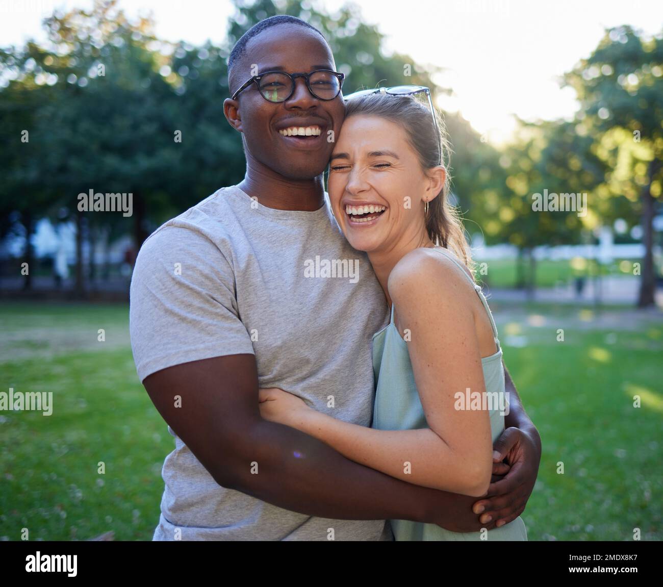 Liebe, Rassenfreunde oder ein paar Freunde umarmen sich bei einem romantischen Date in einem Park und verbinden sich in der Natur miteinander. Romantik, lustiger schwarzer Mann und lachende Frau Stockfoto