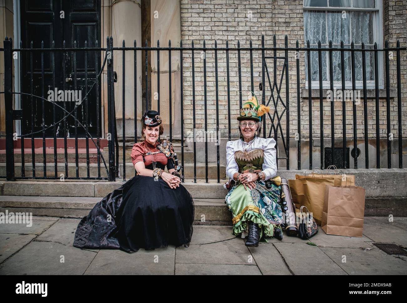 Zwei Steampunks im viktorianischen Stil, die auf einer Treppe in der Straße sitzen. Weiblicher Steampunk in einem historischen Kostüm. Stockfoto