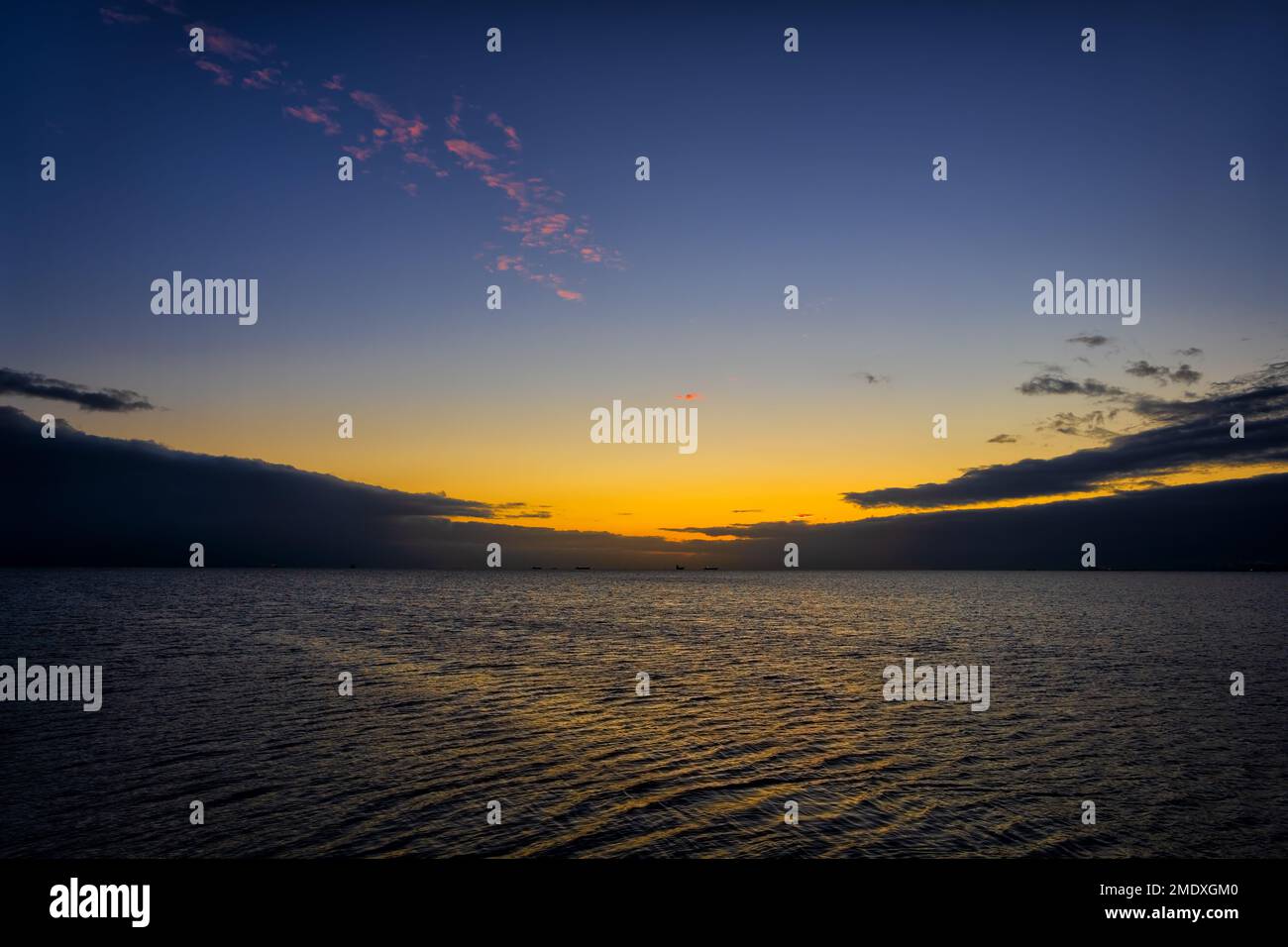 Die Ostsee im Morgengrauen kurz vor Sonnenaufgang. Ruhige Küstenlandschaft mit stürmischen Wolken am Horizont und goldenem Sonnenlicht in der Mitte. Stockfoto