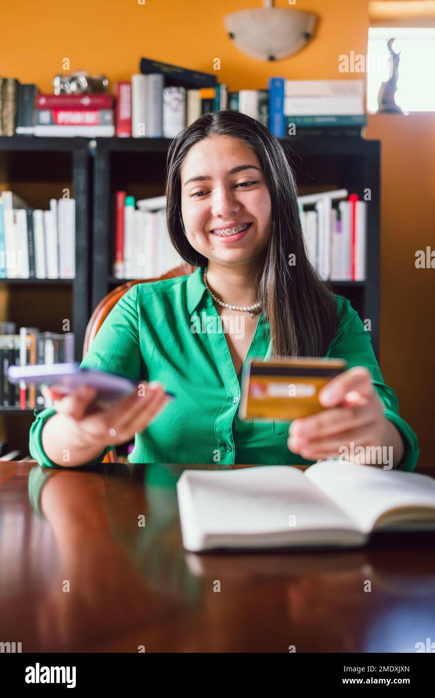 Glückliche junge Frau, die eine Kreditkarte benutzt, um online in ihrer persönlichen Bibliothek einzukaufen. Online-Shopping Stockfoto