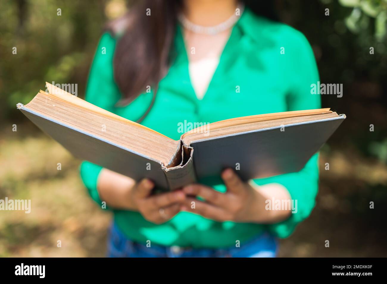 Eine unbekannte Frau mit einer grünen Bluse, die im Garten ein Buch mit Sonnenlicht liest. Weltbuchtag Stockfoto