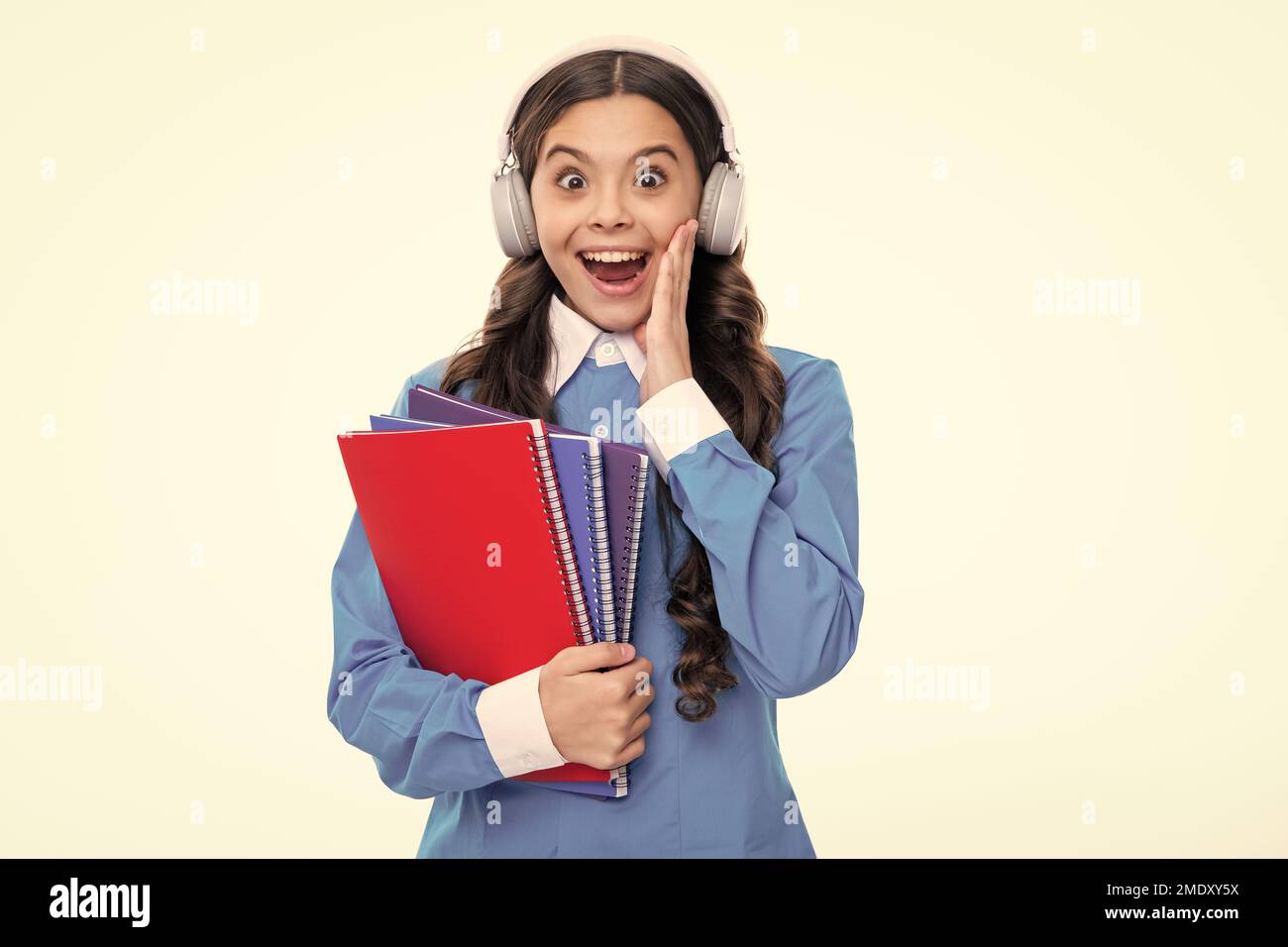 Aufgeregtes Gesicht. Schulkind mit Kopfhörer und Buch isoalted auf weißem Hintergrund. Staunend Ausdruck, fröhlich und froh. Stockfoto