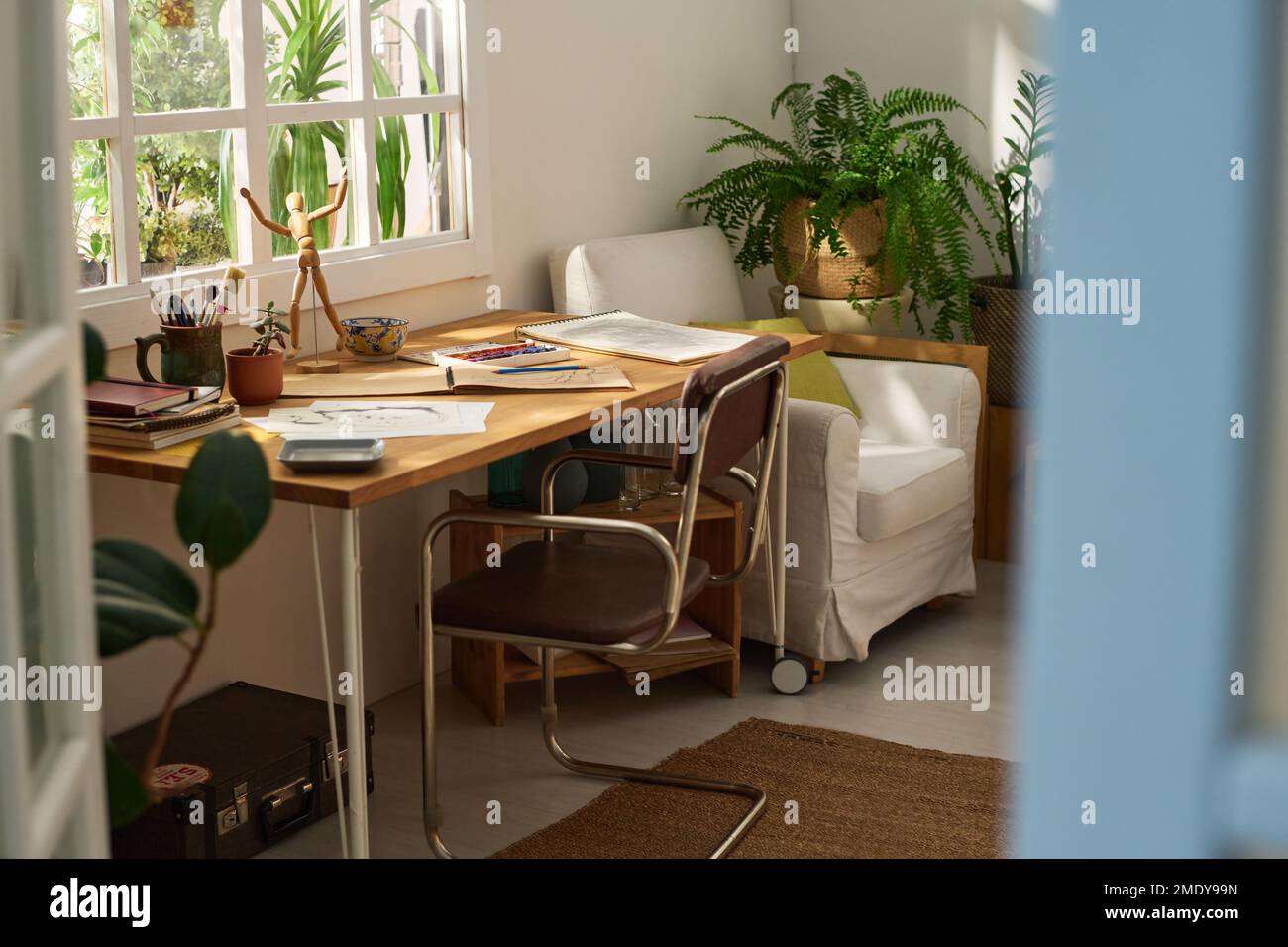 Teil des Zimmers oder Heimstudios eines modernen Künstlers mit Skizzen auf Papieren, Notizblöcken und anderen kreativen Gegenständen auf einem Tisch, der am Fenster steht Stockfoto