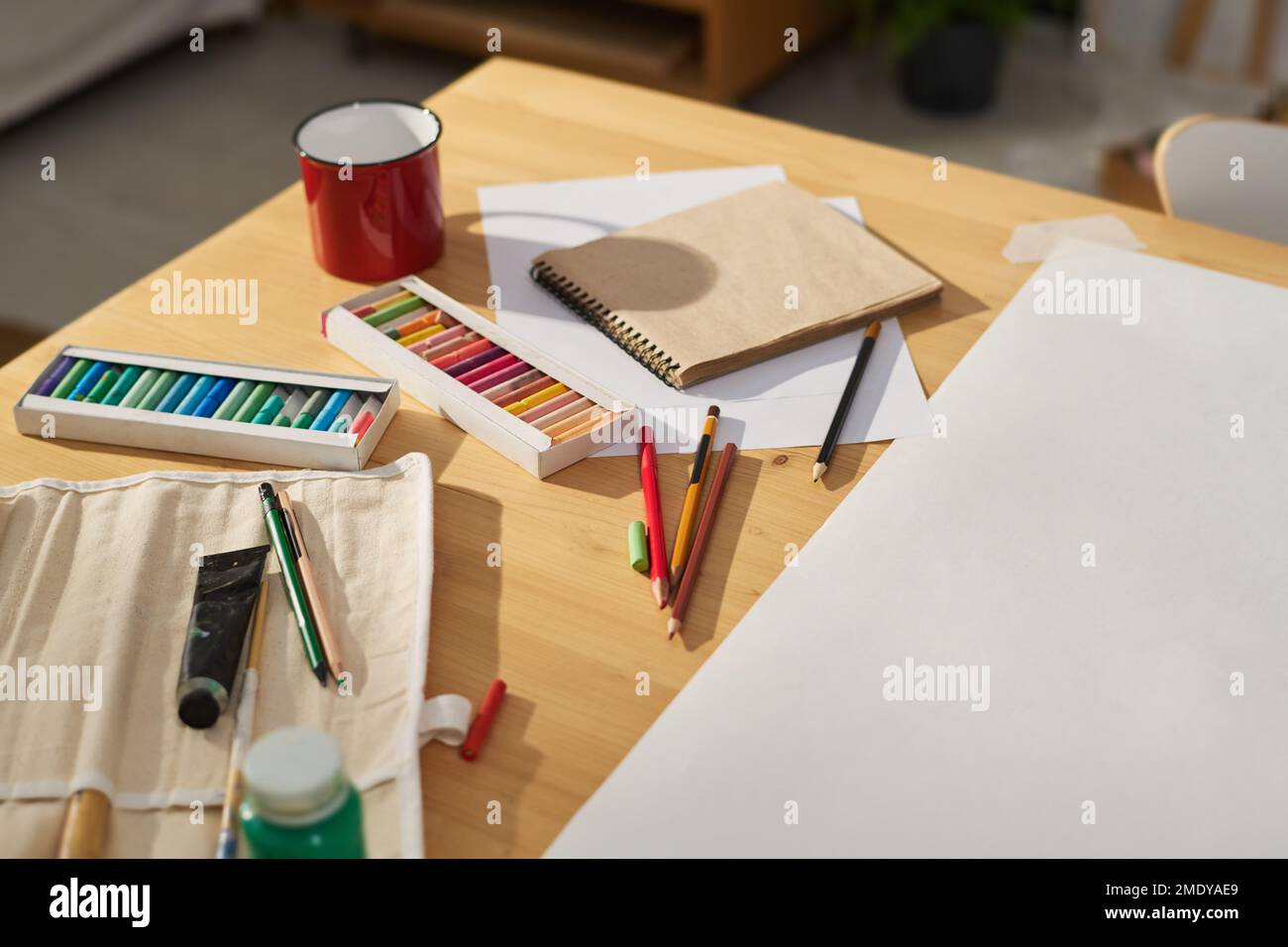 Tischteil mit kleinem Becher, mehrfarbigen Buntstiften, Farben, Notizbuch und leerem Papierbogen zum Zeichnen kreativer Skizzen Stockfoto