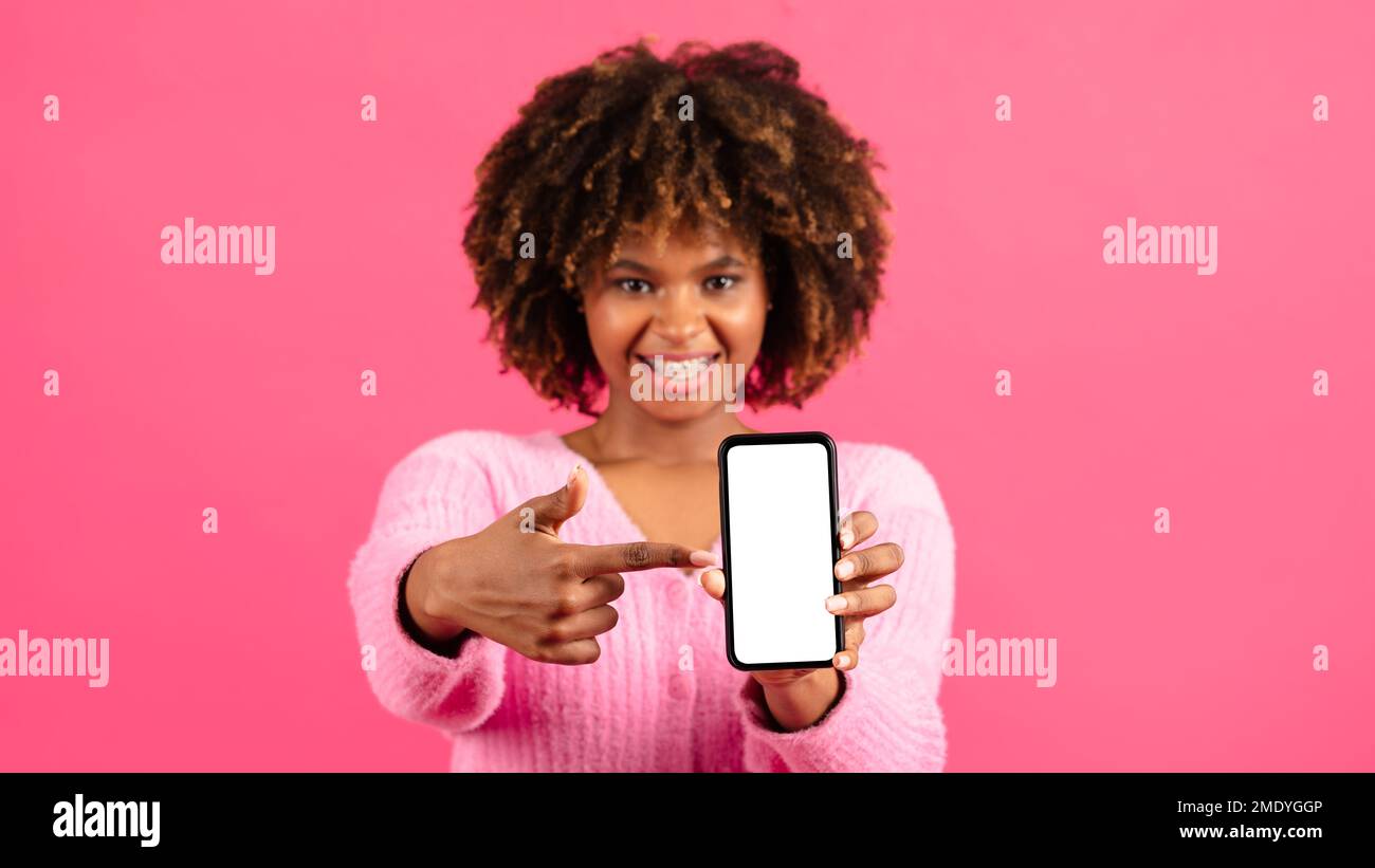 Eine glückliche junge afroamerikanische, lockige Frau mit Zahnspangen zeigt den Finger auf dem Smartphone mit leerem Bildschirm Stockfoto
