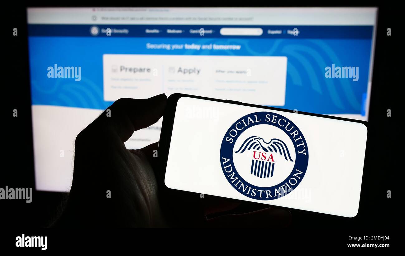 Person, die ein Mobiltelefon mit dem Siegel der US-amerikanischen Sozialversicherungsanstalt (SSA) auf dem Bildschirm vor der Webseite hält. Konzentrieren Sie sich auf das Display des Telefons. Stockfoto Person, die ein Mobiltelefon mit dem Siegel der US-amerikanischen Sozialversicherungsanstalt (SSA) auf dem Bildschirm vor der Webseite hält. Konzentrieren Sie sich auf das Display des Telefons. Stockfoto
