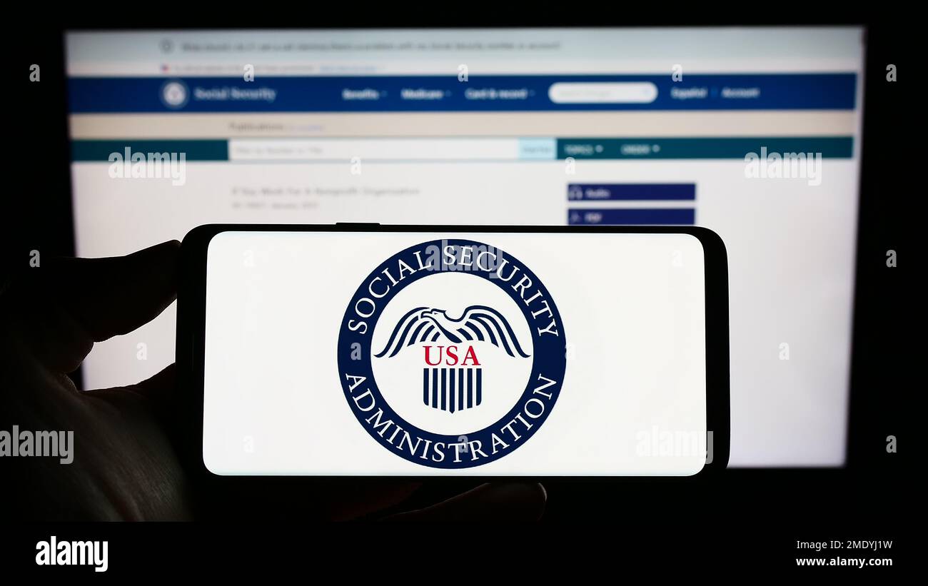 Person, die ein Mobiltelefon mit dem Siegel der US-Sozialversicherungsanstalt (SSA) auf dem Bildschirm vor der Webseite hält. Konzentrieren Sie sich auf das Display des Telefons. Stockfoto Person, die ein Mobiltelefon mit dem Siegel der US-Sozialversicherungsanstalt (SSA) auf dem Bildschirm vor der Webseite hält. Konzentrieren Sie sich auf das Display des Telefons. Stockfoto