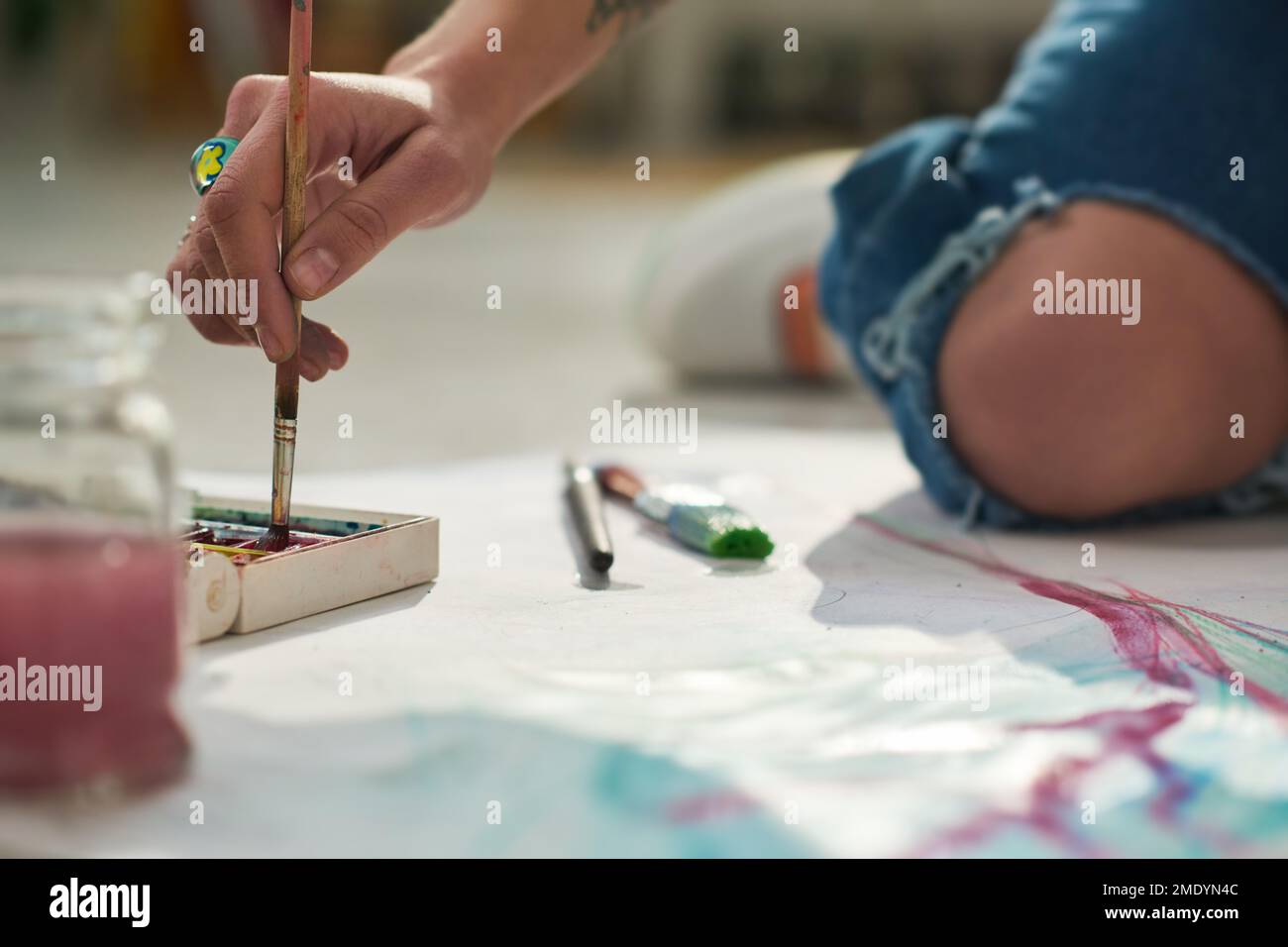 Nahaufnahme der Hand einer jungen Künstlerin mit Pinsel auf dem Boden des Heimstudios und Malen auf Papier mit Wasserfarben Stockfoto