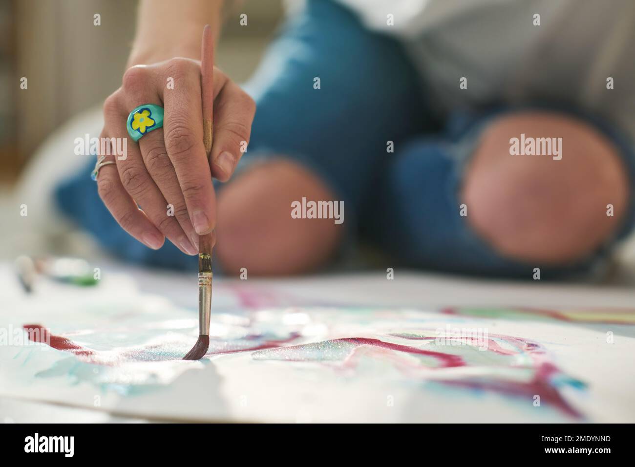 Selektiver Handfokus einer jungen kreativen Kunsthandwerkerin mit Pinsel, die ein neues Kunstwerk auf Papier kreiert, während sie auf dem Boden sitzt Stockfoto